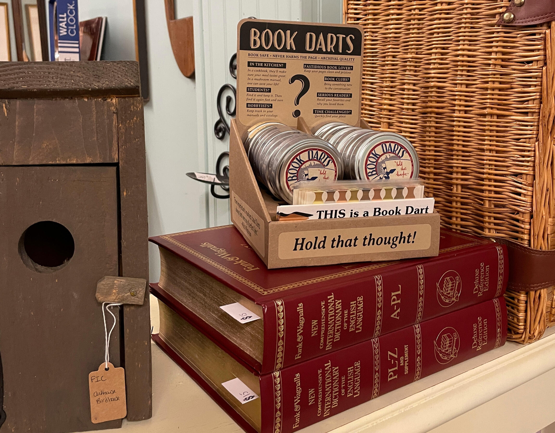 an outhouse shaped birdhouse, a stack of red books, a picnic basket, and a wholesale assortment of "Book Darts"