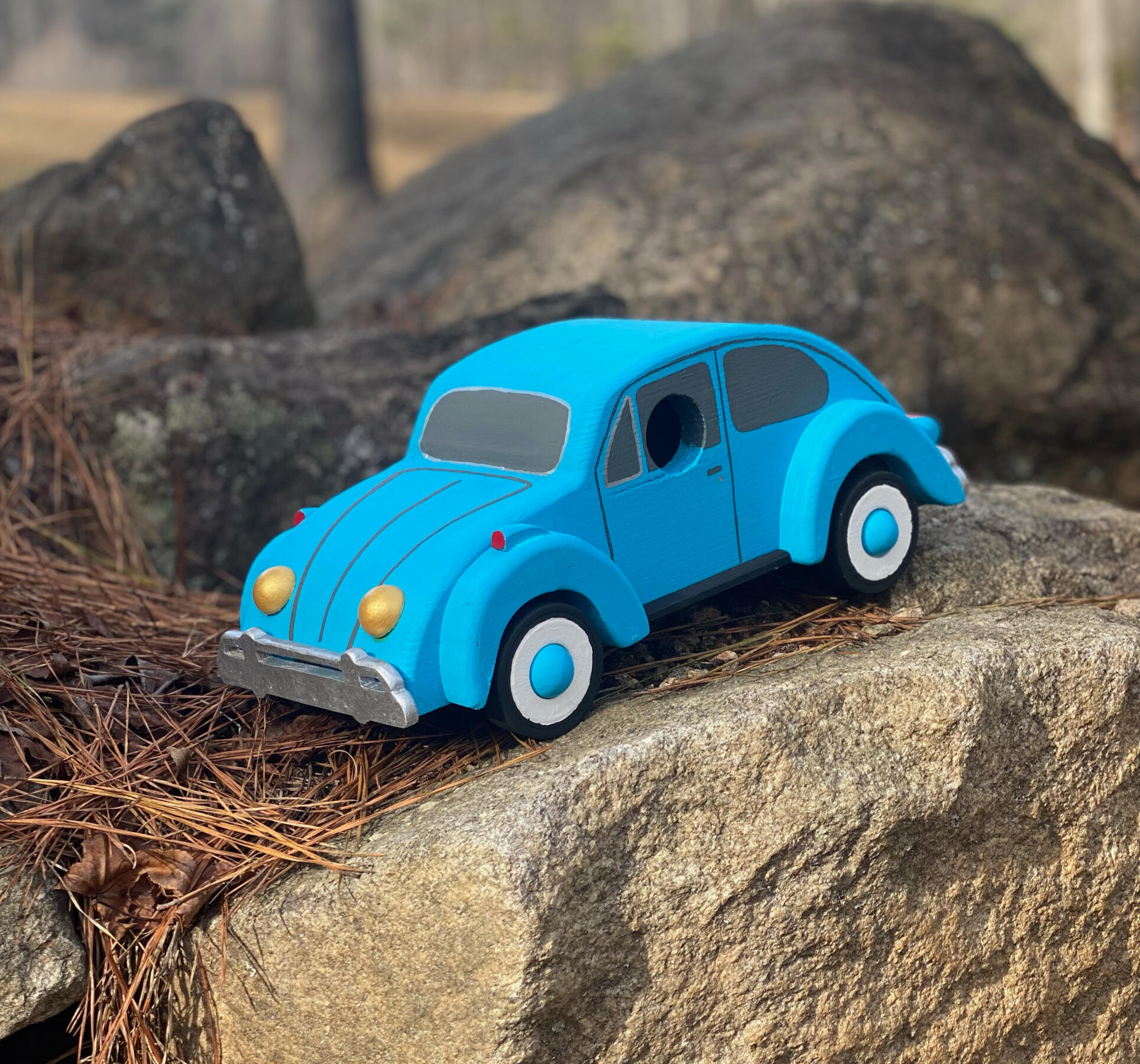 a blue birdhouse in the shape of a VW beetle car, sitting on rocks