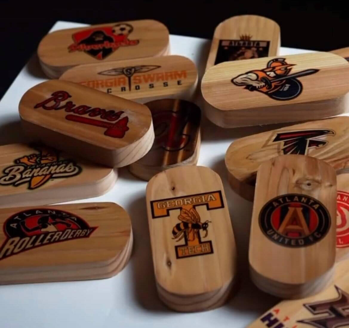 We make custom bottle openers! a pile of pill shaped wooden bottle openers with various Georgia sports teams printed on them