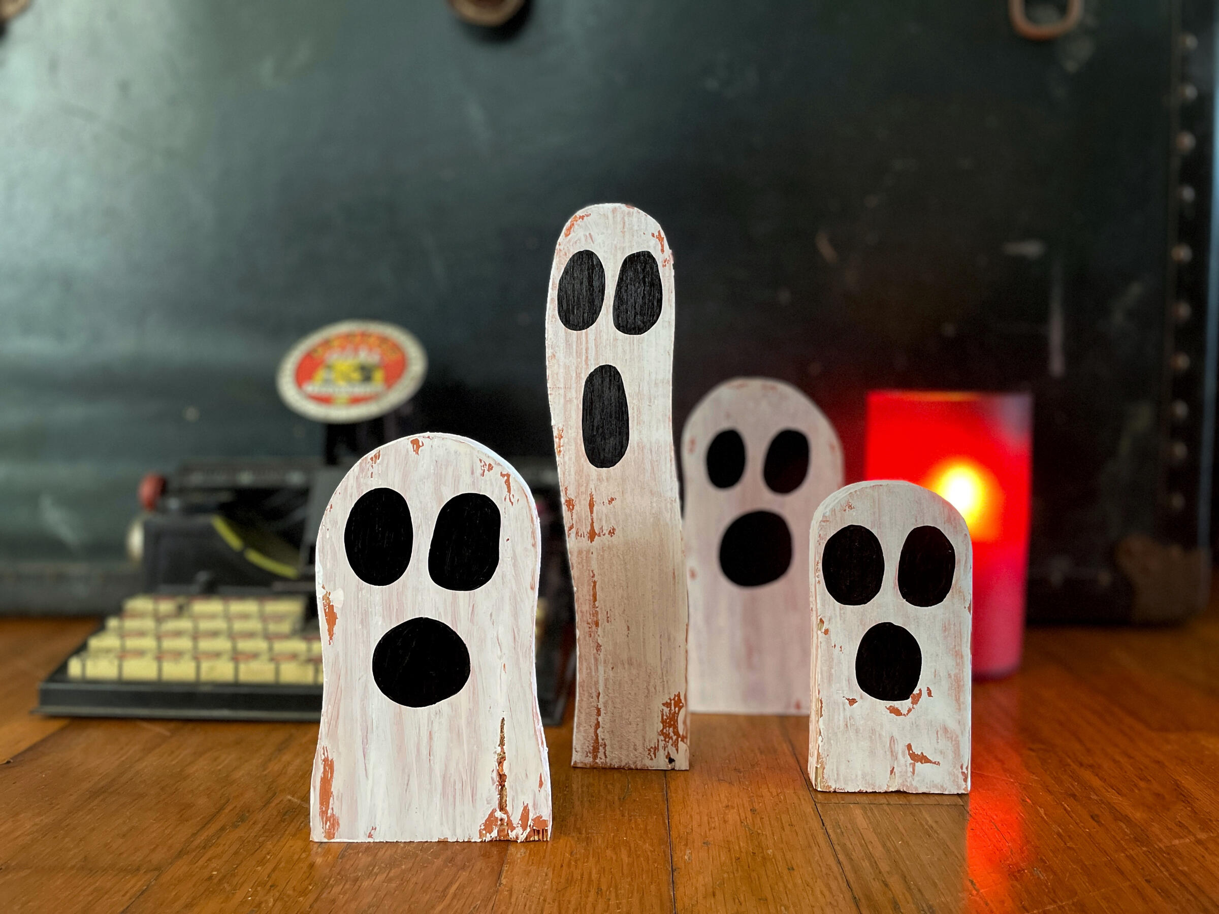 miniature wooden ghosts in front of a candle and vintage typewriter
